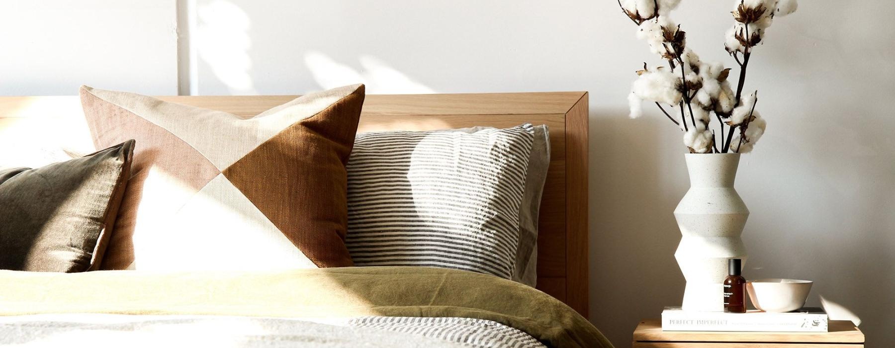 swath of sunlight shines across a well made bed and bedside table with a vase of cotton plants